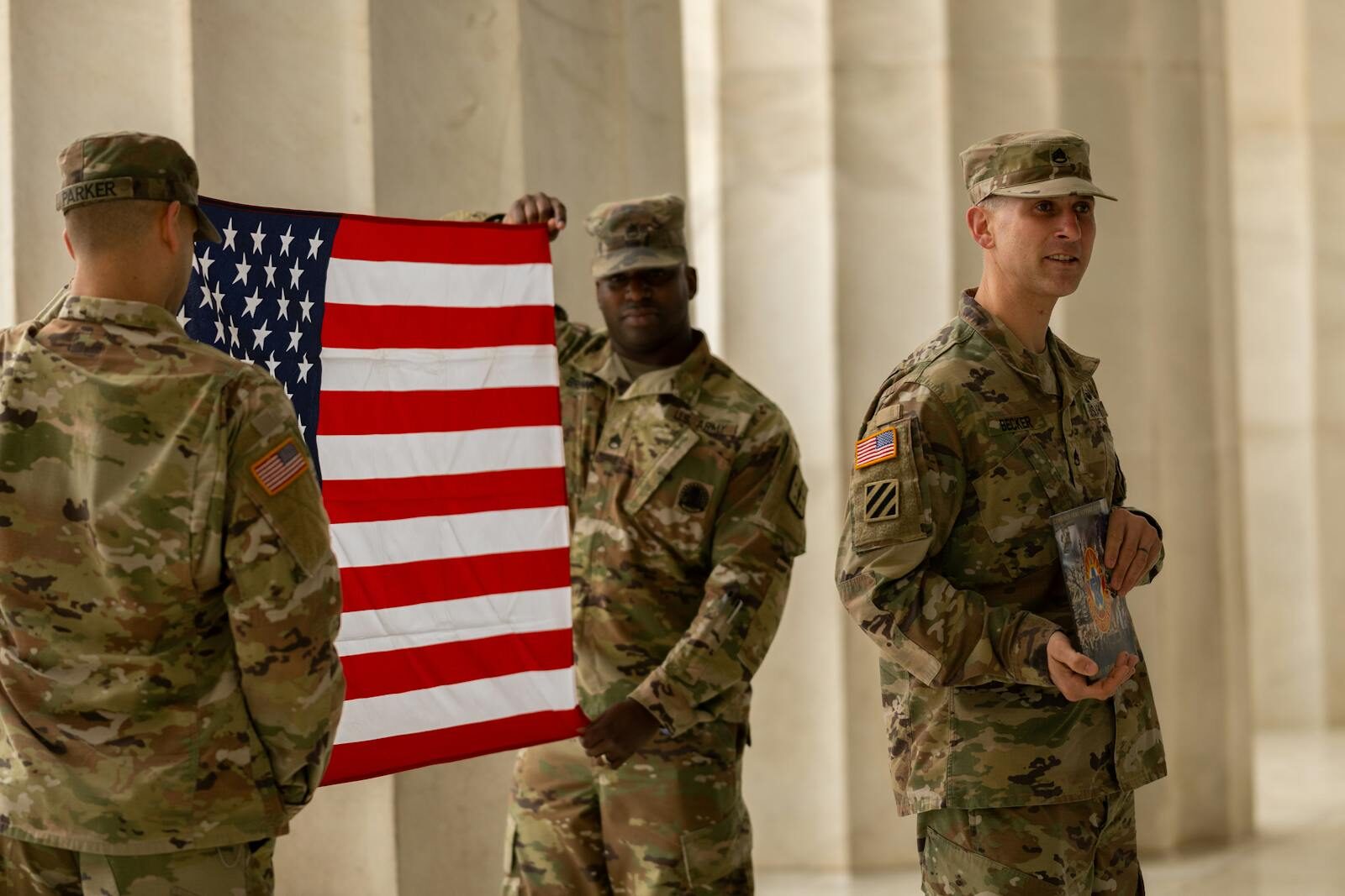 US soldiers in camouflage uniforms hold American flag at Washington DC landmark.