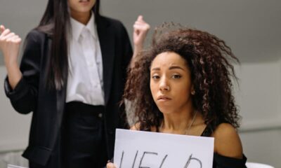 A woman holding a help sign, depicting workplace harassment in an office setting.