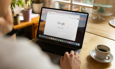 An adult using a laptop indoors, browsing Google at a wooden table with coffee.