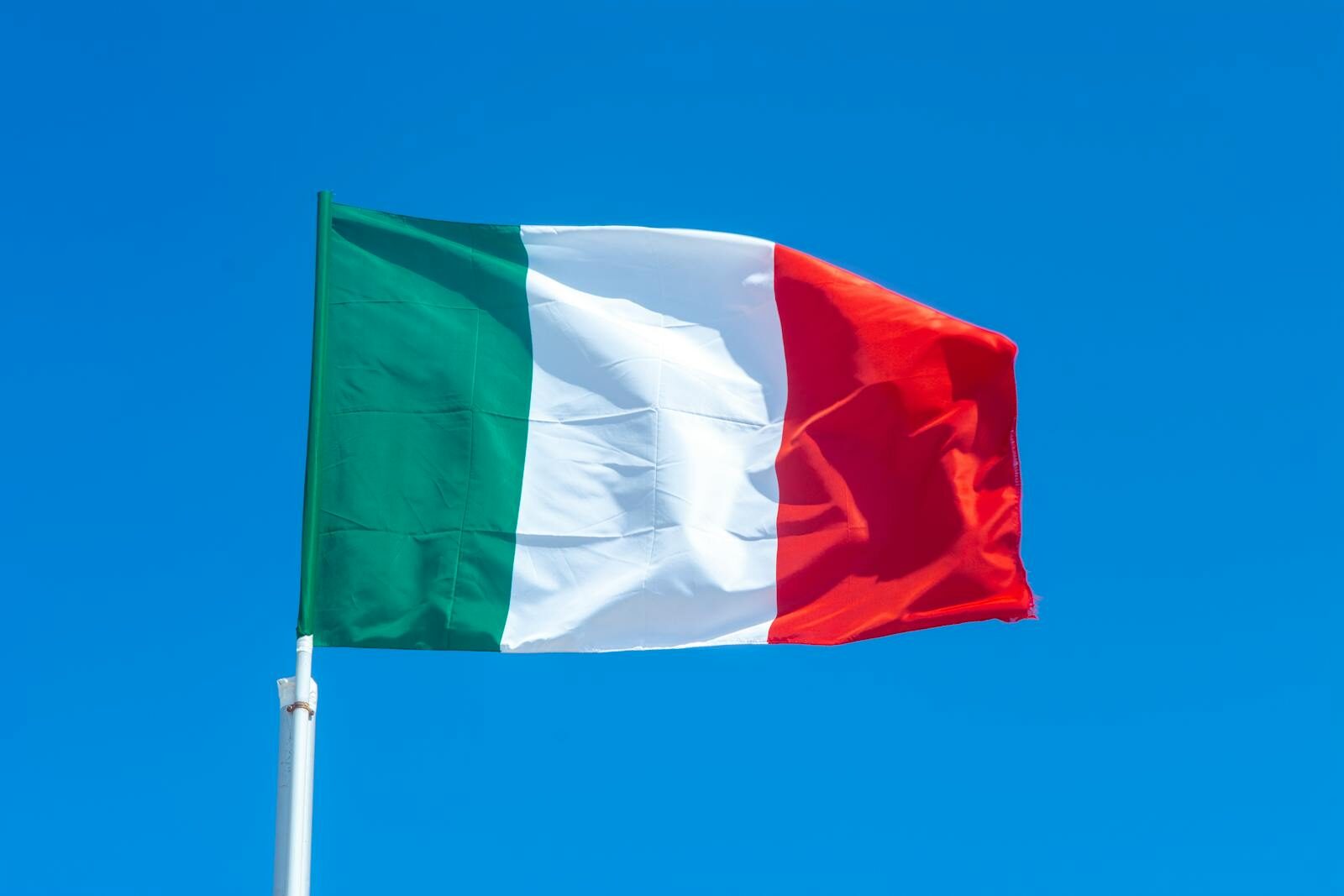 The Italian flag waves vibrantly against a clear blue sky, symbolizing national pride.