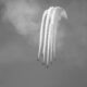 Black and white image of an aircraft formation with contrails against a cloudy sky.