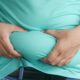 Close-up of hands gripping an overweight belly, depicting body fat focus.