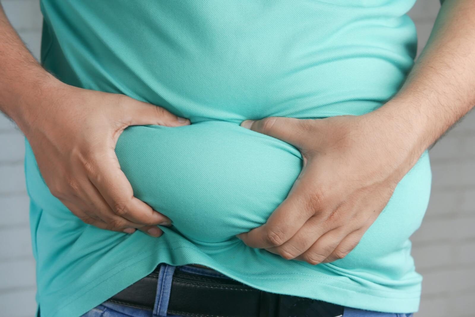 Close-up of hands gripping an overweight belly, depicting body fat focus.
