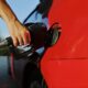 Close-up of a person refueling a red car at an outdoor gas station during the day.