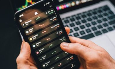 Hands holding smartphone with stock app, laptop displaying charts. Perfect for financial and technology themes.