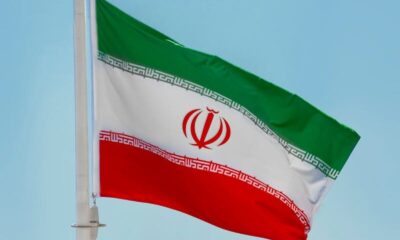 Low-angle view of the Iranian flag waving on a flagpole against a clear blue sky in Tehran, Iran.