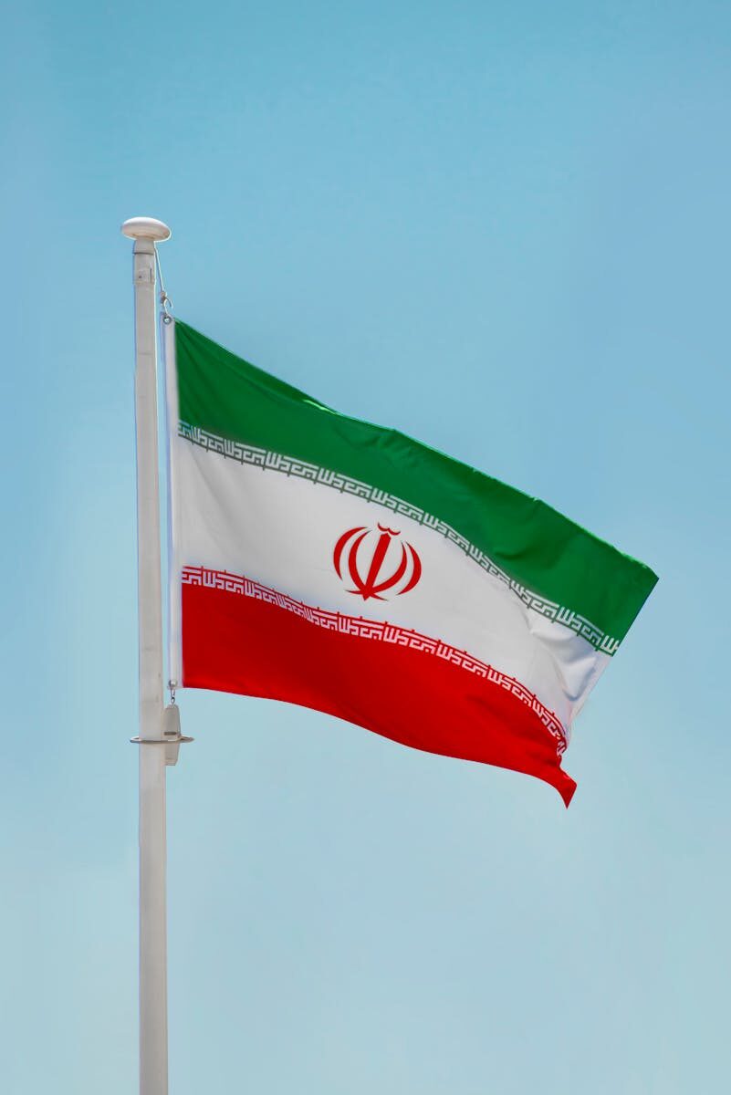 Low-angle view of the Iranian flag waving on a flagpole against a clear blue sky in Tehran, Iran.