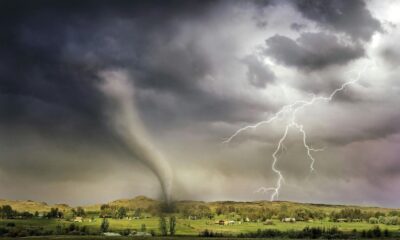 A powerful tornado and vibrant lightning striking over a rural countryside landscape.