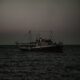 A fishing boat sails on the open sea at twilight, with dim lighting capturing a serene maritime scene.