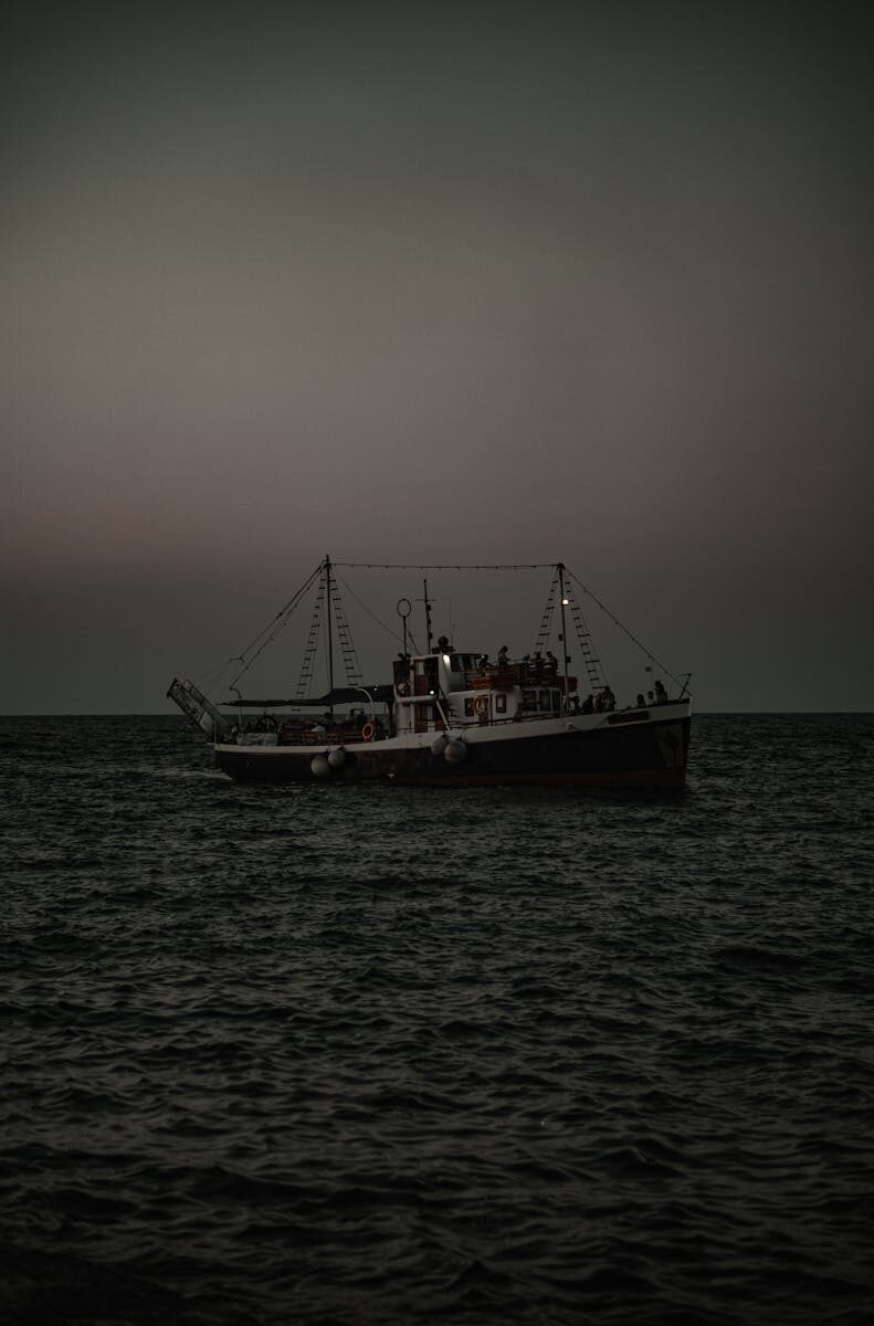 A fishing boat sails on the open sea at twilight, with dim lighting capturing a serene maritime scene.