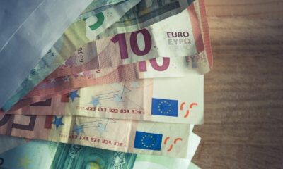 A collection of Euro banknotes emerging from an envelope on a wooden surface.