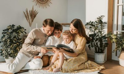 A joyful family shares a book indoors, surrounded by houseplants, promoting reading and togetherness.
