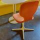 Contemporary orange chair with round table against yellow bench, showcasing modern interior décor.