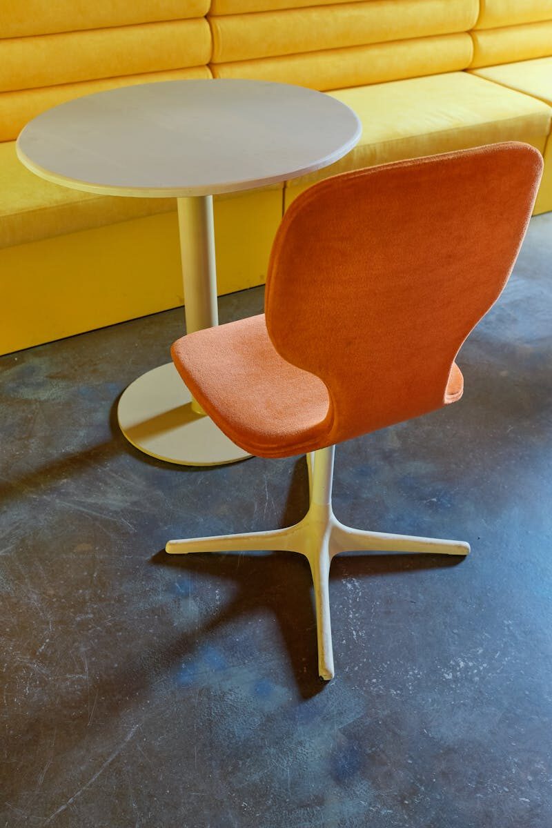 Contemporary orange chair with round table against yellow bench, showcasing modern interior décor.