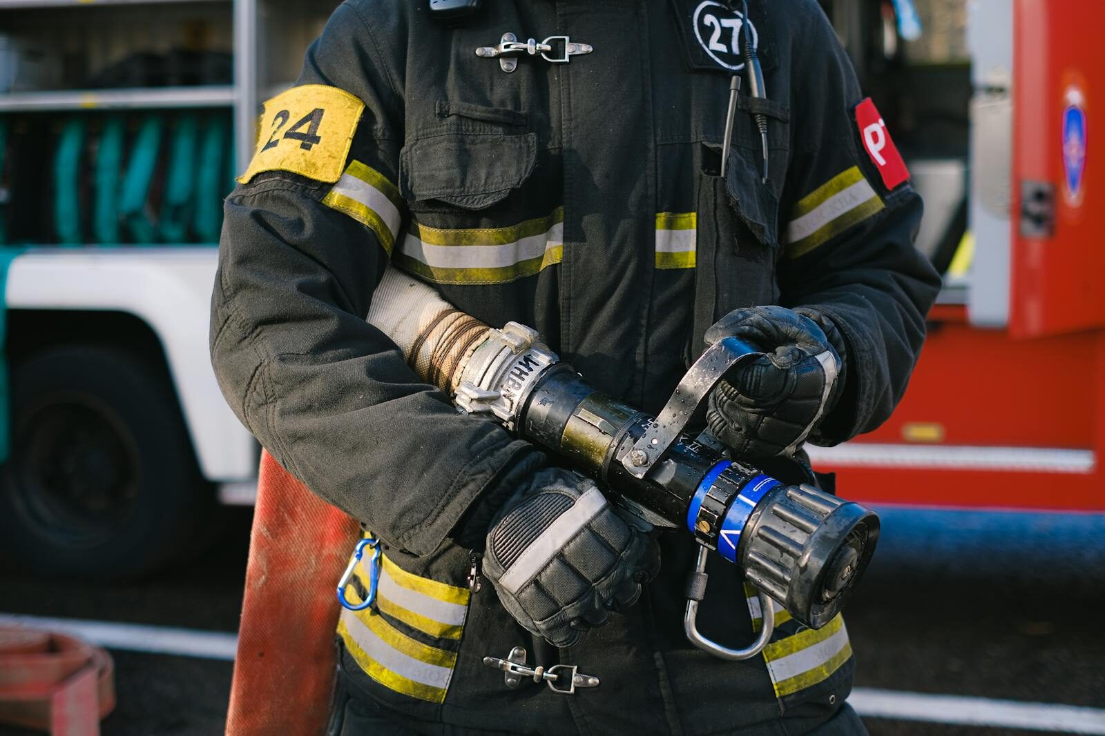 Firefighter in protective gear holding a hose nozzle, ready for action.