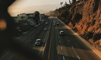 From above of contemporary cars driving on smooth surface of roadway near hills and houses