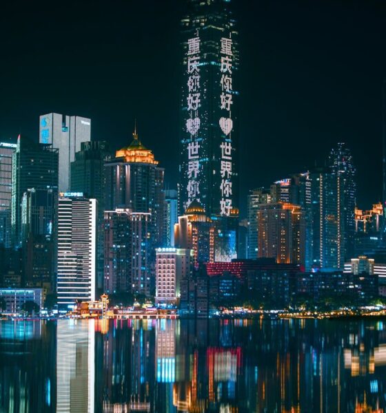 Chongqing skyline illuminated at night with neon lights reflecting on the river, showcasing urban futuristic architecture.