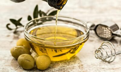 Close-up of olive oil being poured into a glass bowl surrounded by fresh olives and kitchen tools.