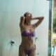 Slim young lady in swimsuit taking spacious shower next to swimming pool in resort