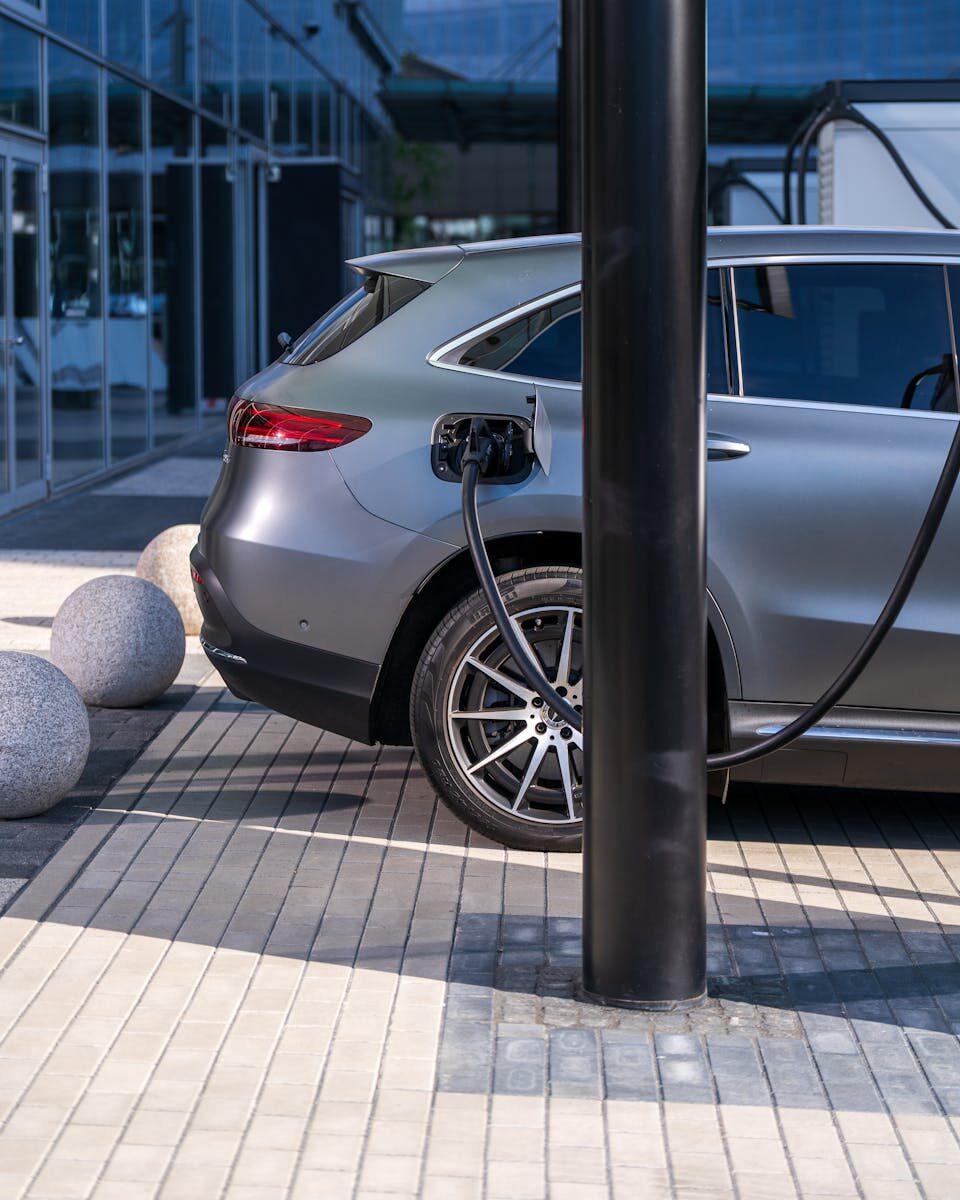 A silver electric car charging at an urban station, highlighting sustainable living in a modern cityscape.