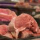 Close-up of fresh raw pork cuts on display in a glass case at a market.