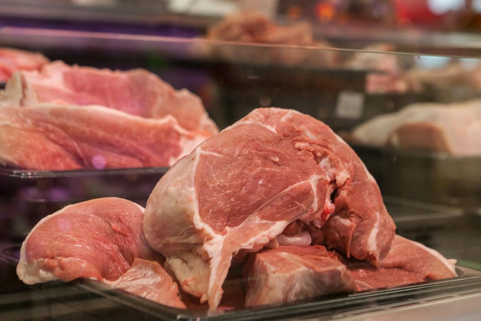 Close-up of fresh raw pork cuts on display in a glass case at a market.