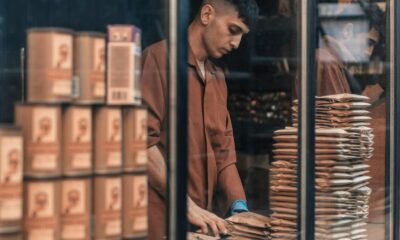A man packing goods behind a glass window, showcasing a work environment with reflections and stacked items.