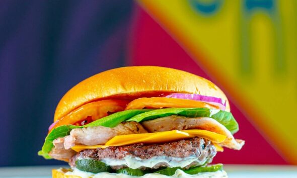 An appetizing burger with cheese, lettuce, tomato, and onions against a colorful background.