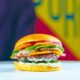 An appetizing burger with cheese, lettuce, tomato, and onions against a colorful background.