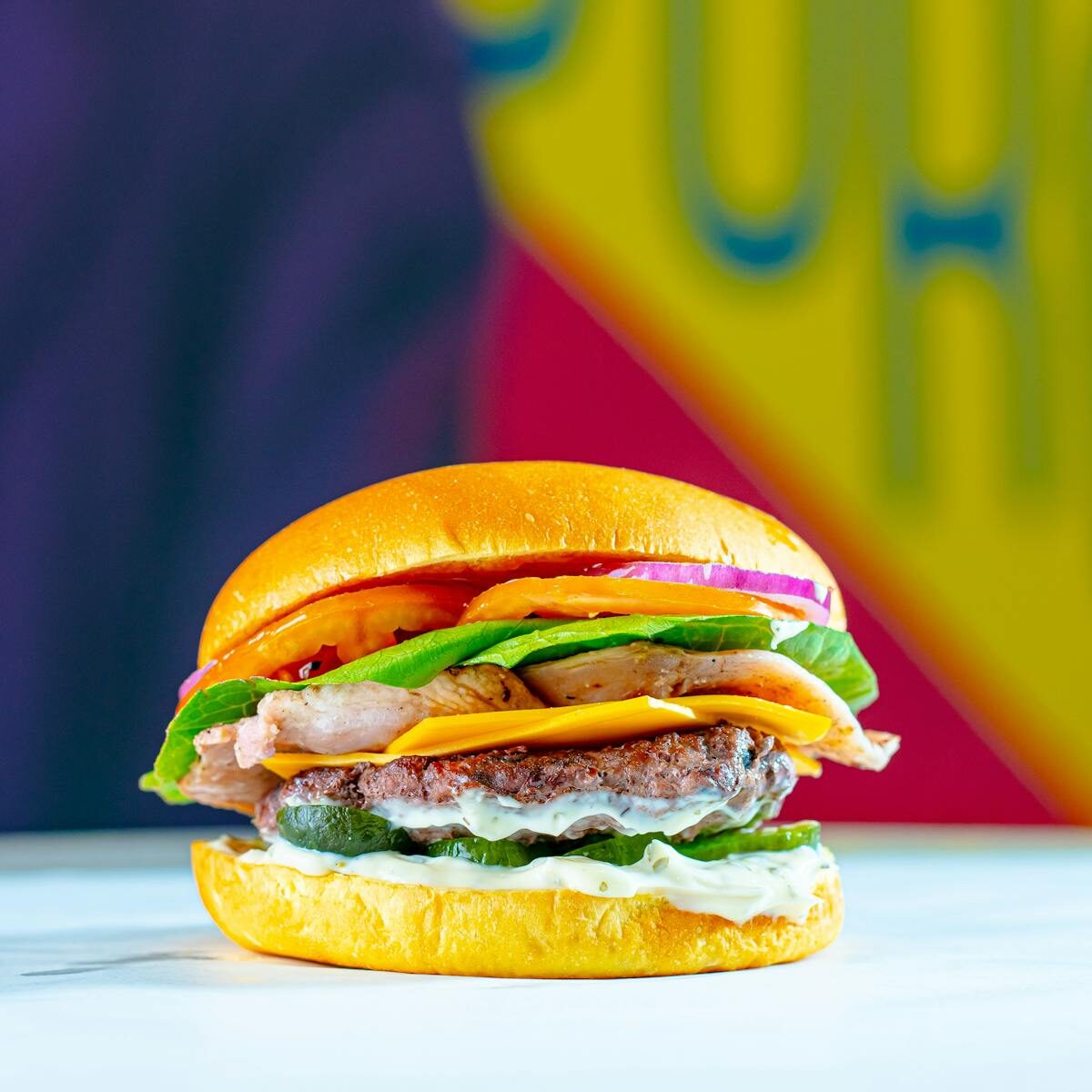An appetizing burger with cheese, lettuce, tomato, and onions against a colorful background.