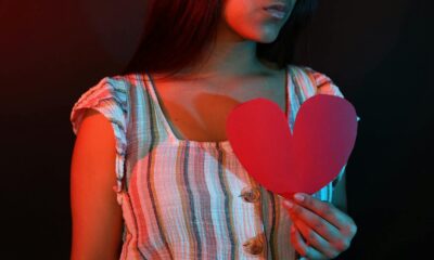 Young woman holding a red paper heart, portrayed in dramatic red and blue lighting.
