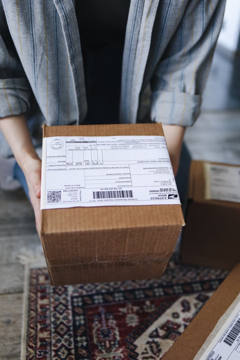 Close-up of a person holding a cardboard box with shipping labels, ideal for delivery logistics visuals.