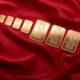 Array of fine gold bars displayed on rich red fabric, symbolizing wealth and luxury.