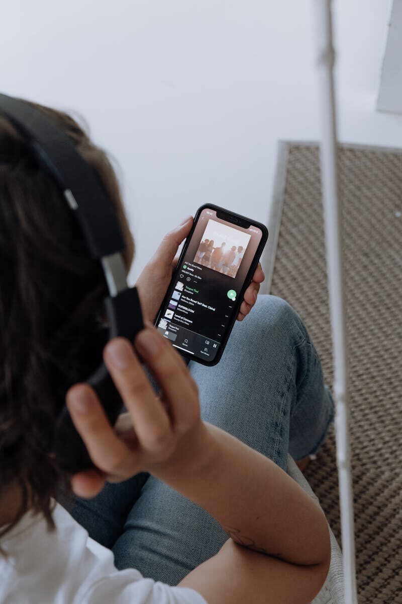 A young woman wearing headphones, relaxing at home, listens to music on her smartphone.