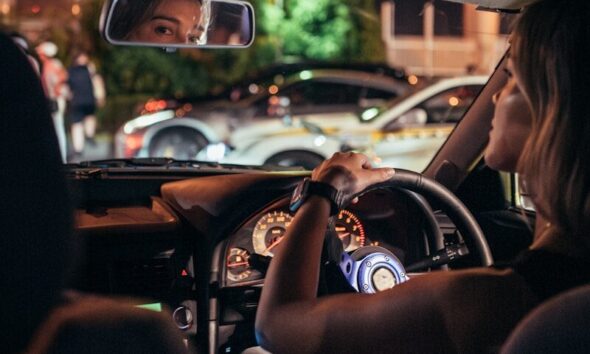 Woman driving car at night with city lights reflection