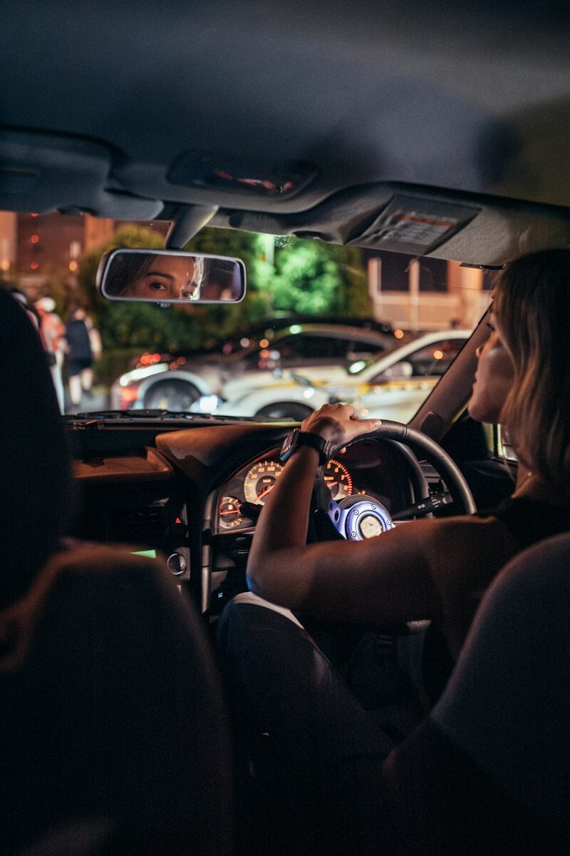 Woman driving car at night with city lights reflection