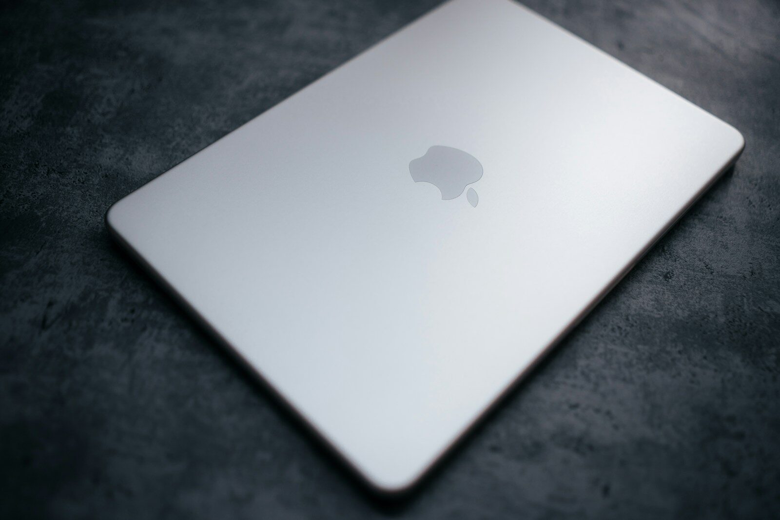 Closed silver laptop with apple logo on dark surface