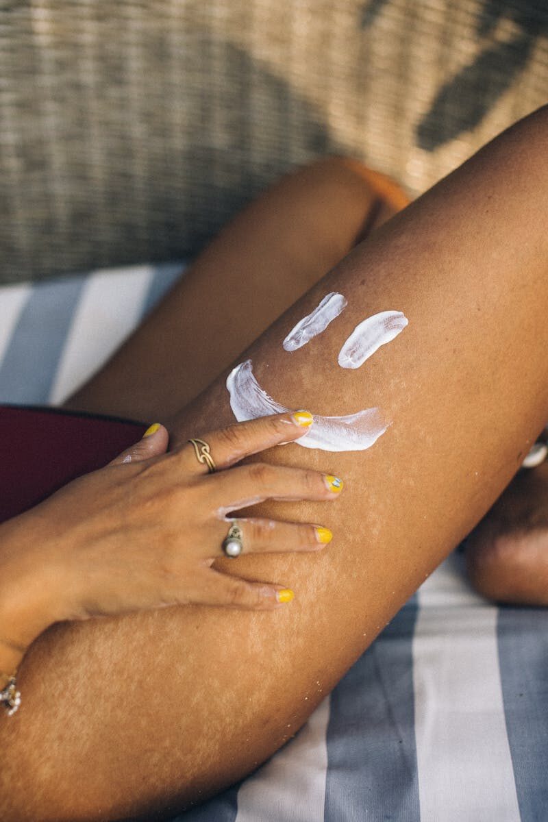 Close-up of a hand applying sunscreen on a leg with a smiley. Sunny and fun outdoor setting.