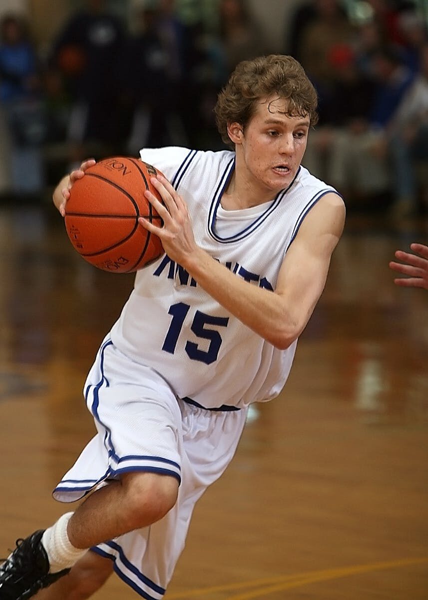 Teen male basketball player in action on indoor court during a game.