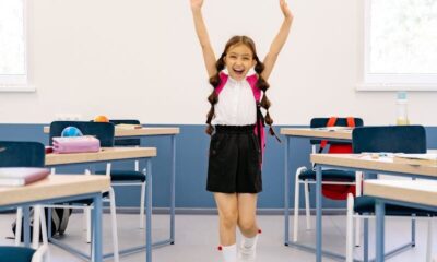 Happy girl with arms raised in a bright classroom, exuding positivity and excitement.