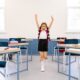 Happy girl with arms raised in a bright classroom, exuding positivity and excitement.