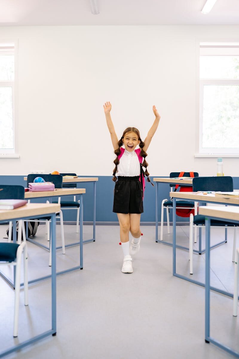 Happy girl with arms raised in a bright classroom, exuding positivity and excitement.
