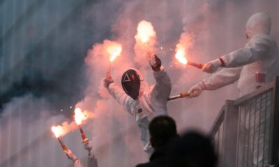 Masked figures hold flares, creating a smoky atmosphere.