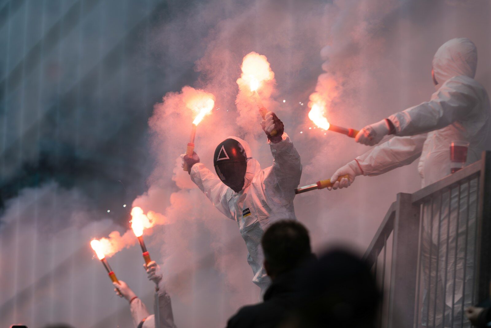 Masked figures hold flares, creating a smoky atmosphere.