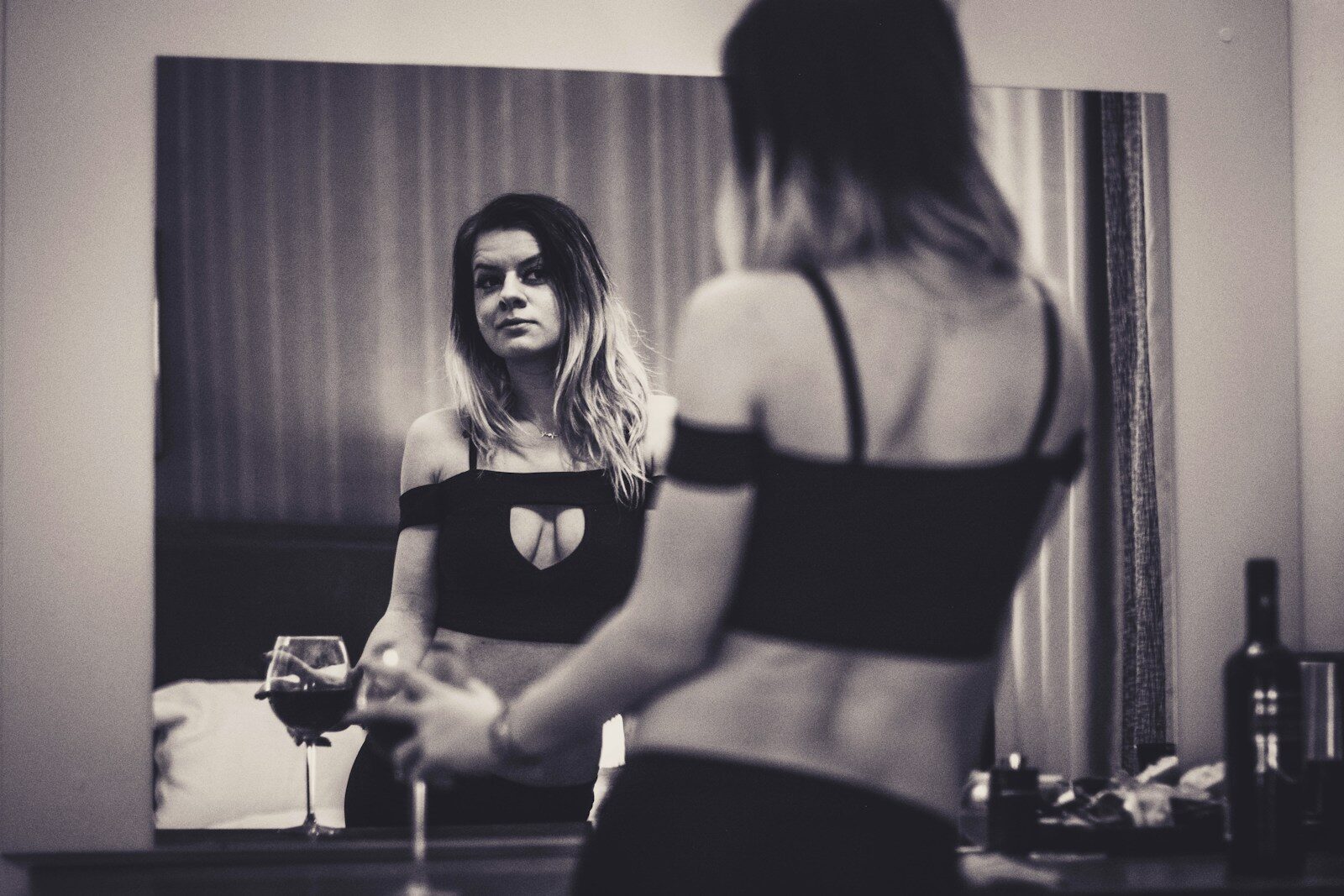 a woman standing in front of a mirror holding a wine glass