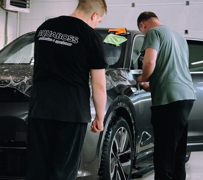 Two men detailing a car in an indoor workshop, focusing on precision and care.