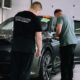 Two men detailing a car in an indoor workshop, focusing on precision and care.