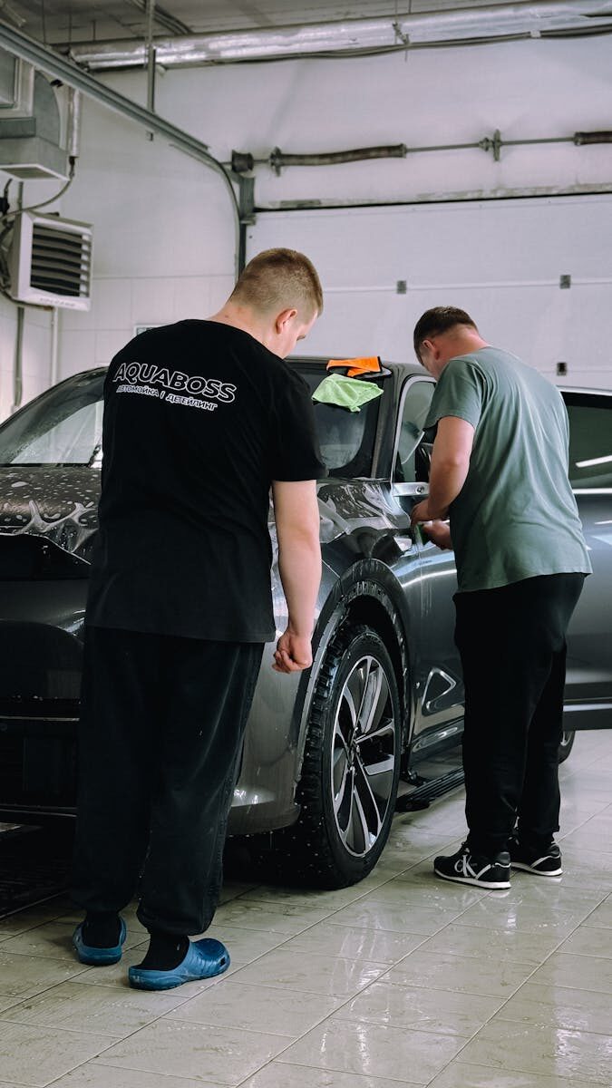 Two men detailing a car in an indoor workshop, focusing on precision and care.