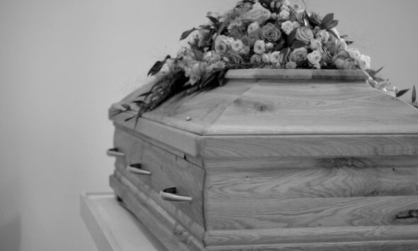 Black and white photo of a wooden coffin adorned with a detailed floral arrangement.