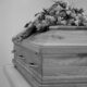 Black and white photo of a wooden coffin adorned with a detailed floral arrangement.